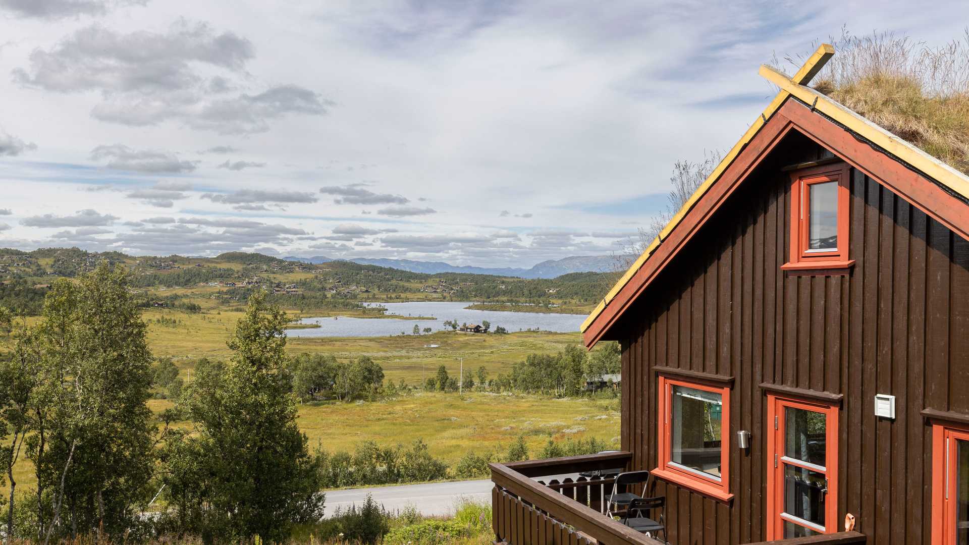 Fjellhytte med torvtak ved innsjø og skog i vakker norsk natur.