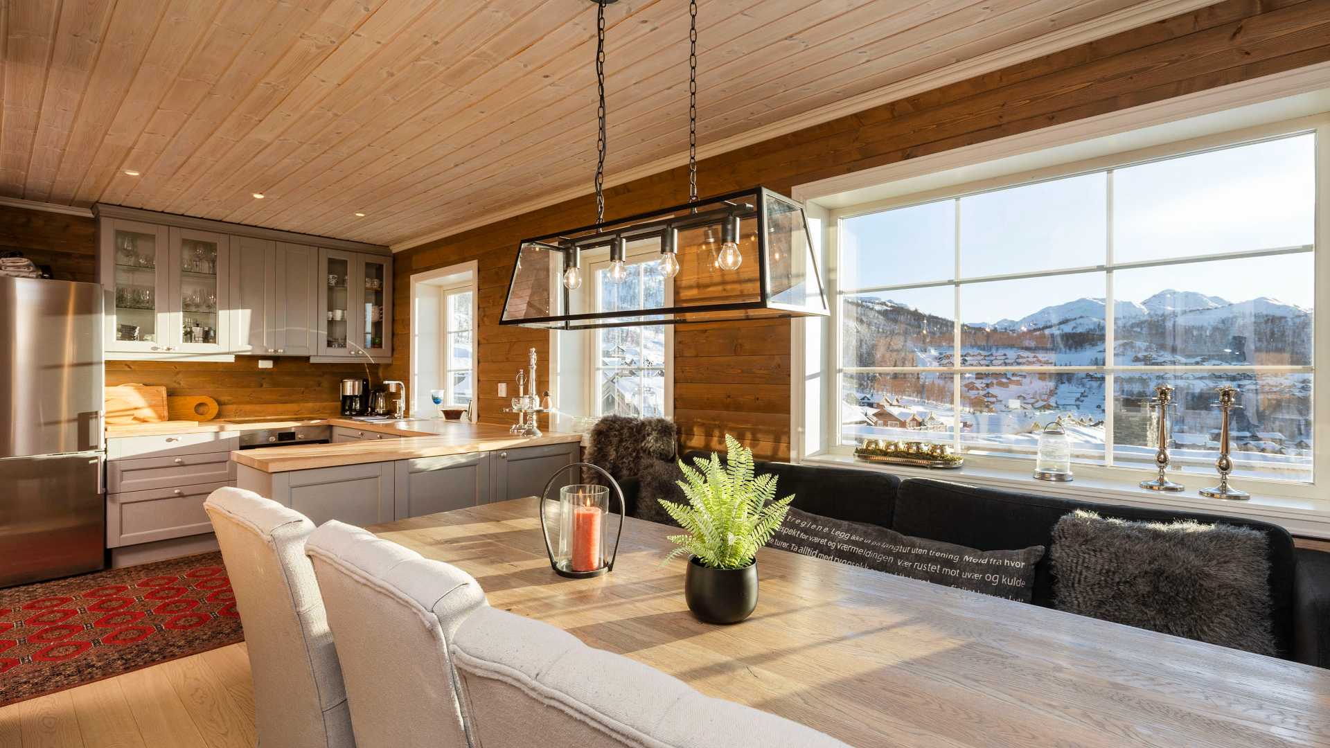 Lyst kjøkken med trepanel, stor vindu og fjordutsikt. Moderne innredning med grå skap og spisebord.