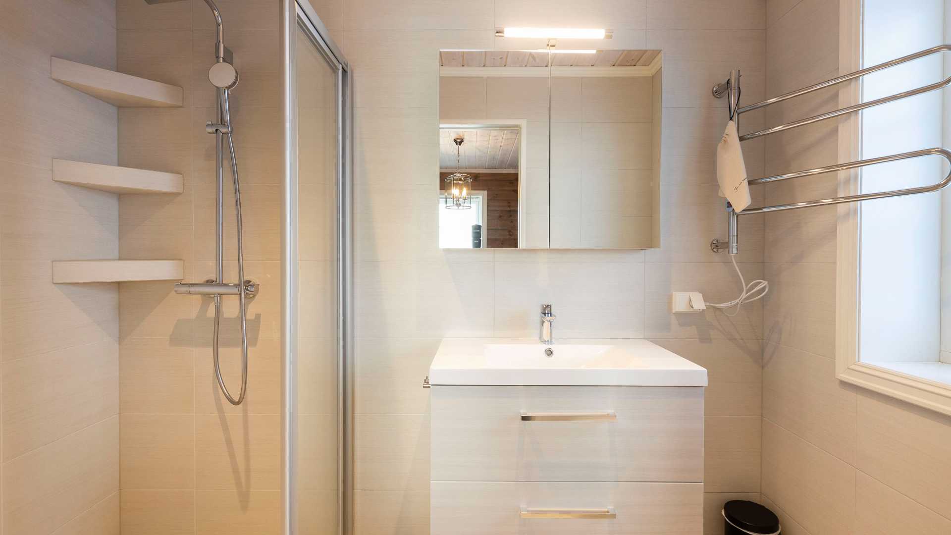 Moderne bad med dusj, vask, speil, og håndkletørker i lyst interiørdesign.