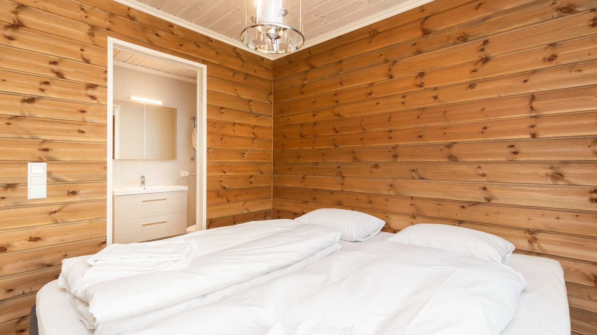 Soverom med trepanel og myk seng, tilstøtende bad i lys farge med moderne armatur.