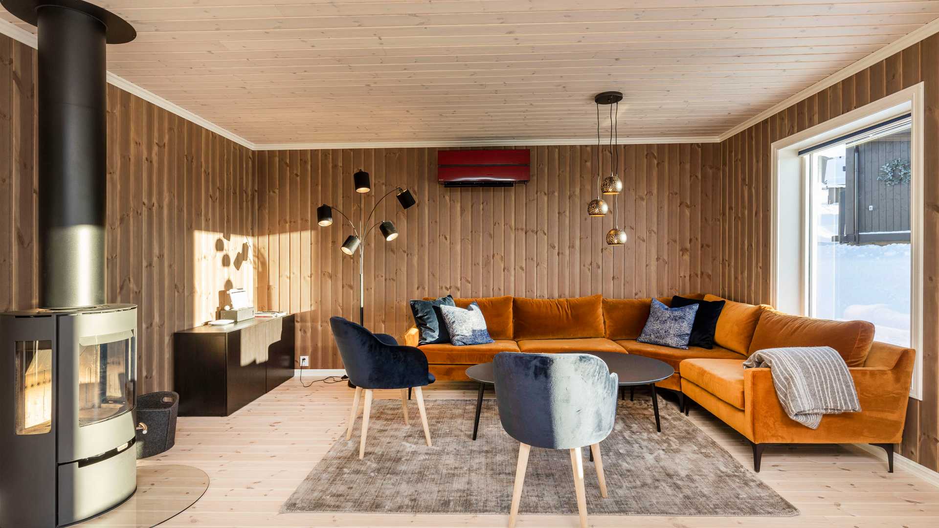 Lun stue med oransje sofa, vedovn og moderne belysning, gir et koselig og stilfullt interiørdesign.