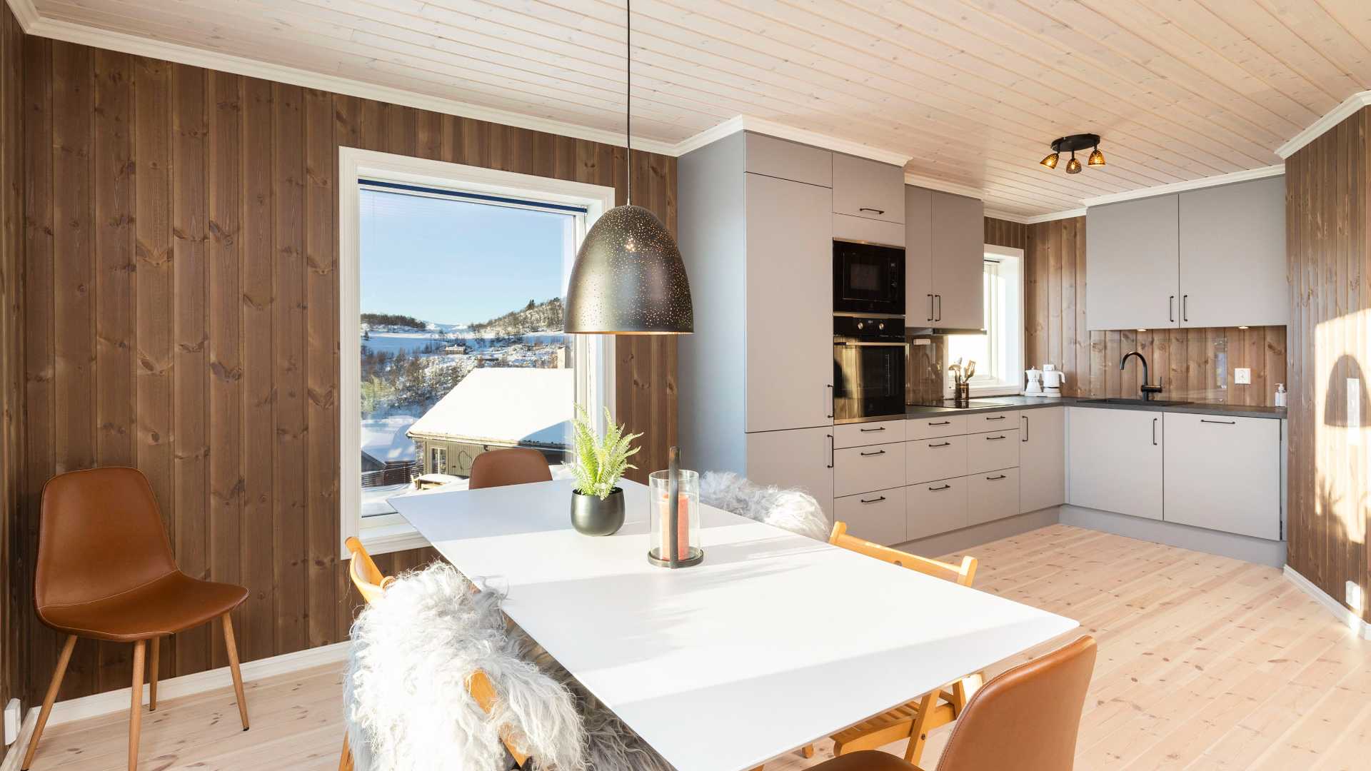Moderne kjøkkeninteriør med trepanel, dagslys og fjellutsikt gjennom vindu. Skandinavisk design, elegante detaljer.