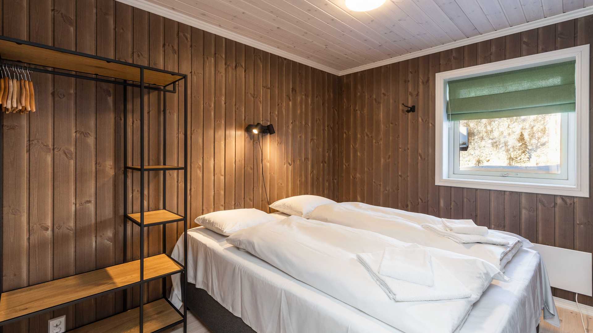 Koselig soverom med hvitt sengetøy, brune panelvegger og hylle i tre og metall.