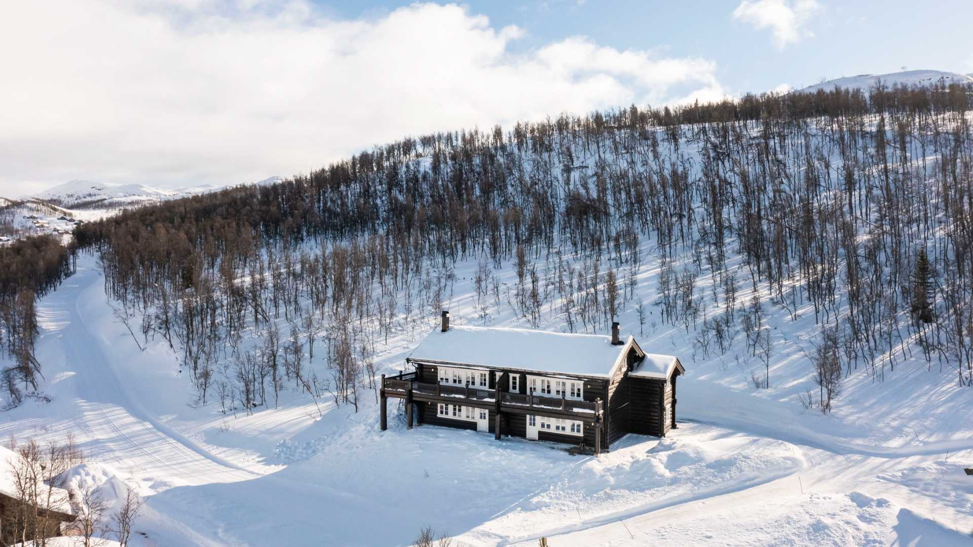 Stor fjellhytte omringet av snødekte landskap og trær. Perfekt for vinterferie i norsk natur.