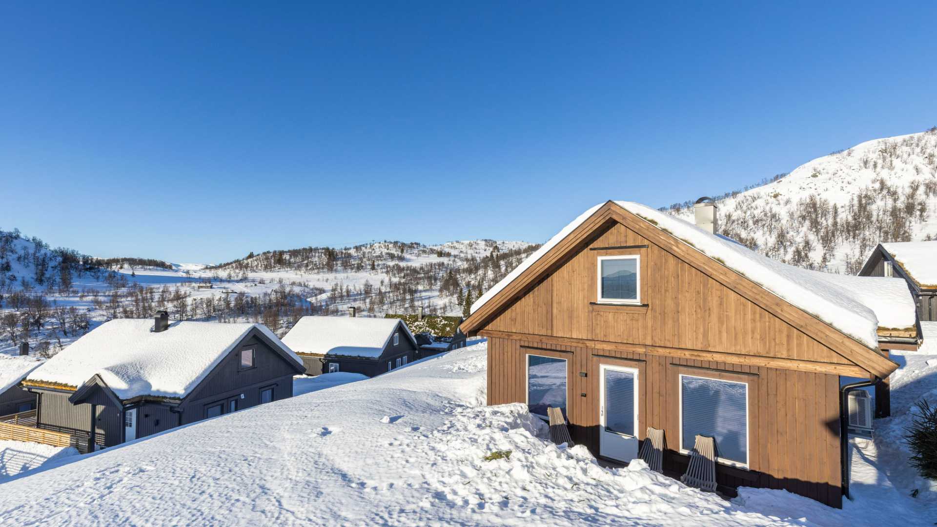 Snødekte hytter i norsk fjellandskap under klar blå himmel.