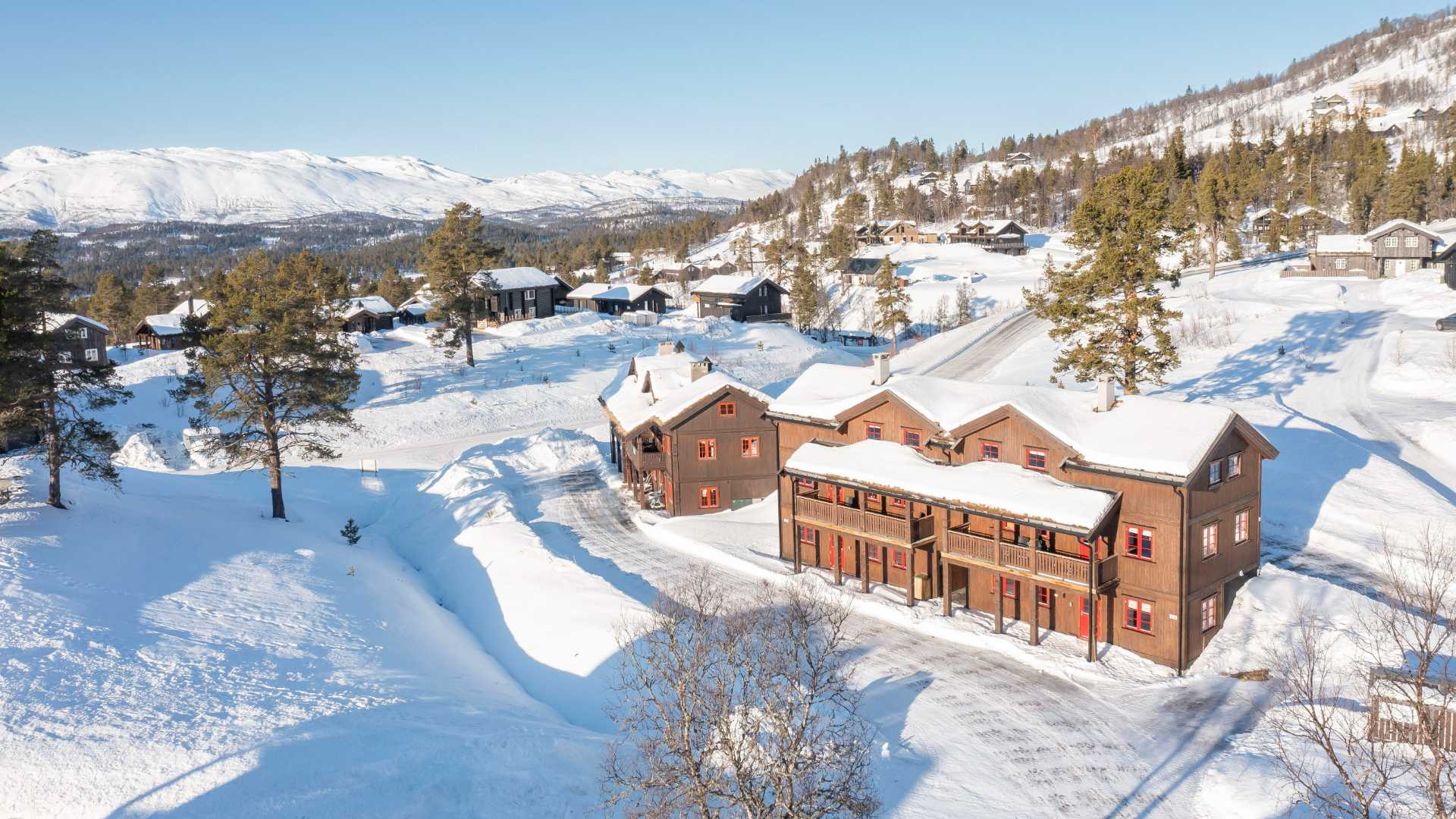 Vinterlandskap med hytter i snødekt fjellområde under klar blå himmel.