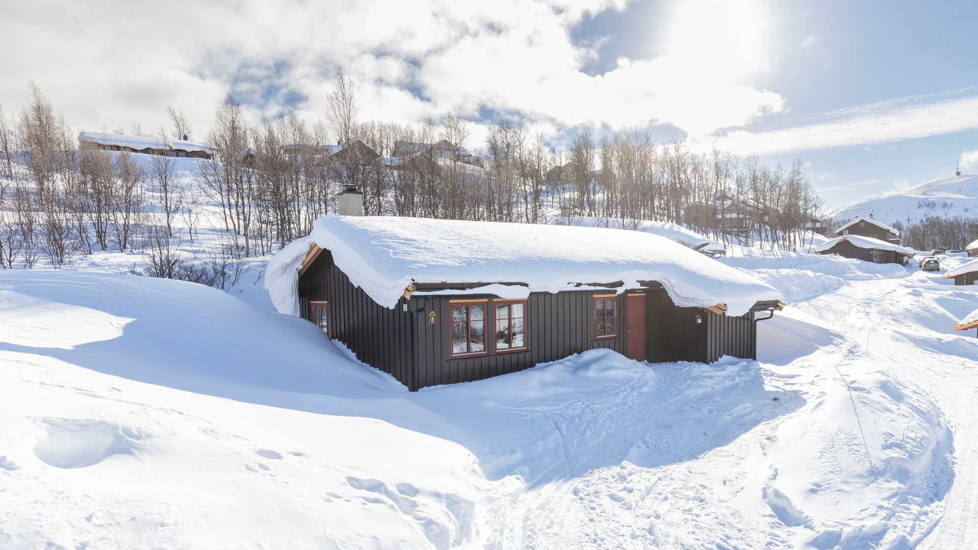 Snødekket hytte i norsk vinterlandskap med solrik bakgrunn. Perfekt for fjellferier og avslapning.