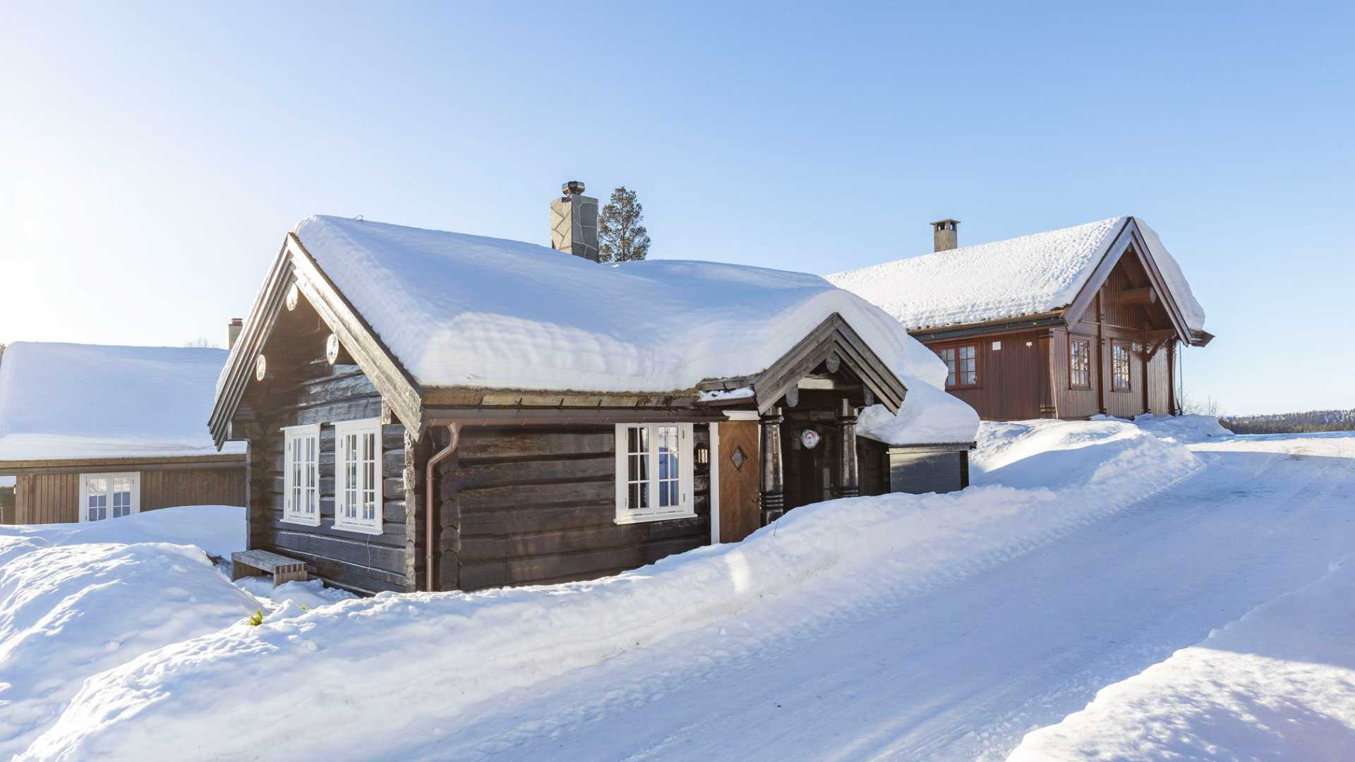 Tradisjonell norsk hytte dekket av snø på en solrik dag om vinteren.