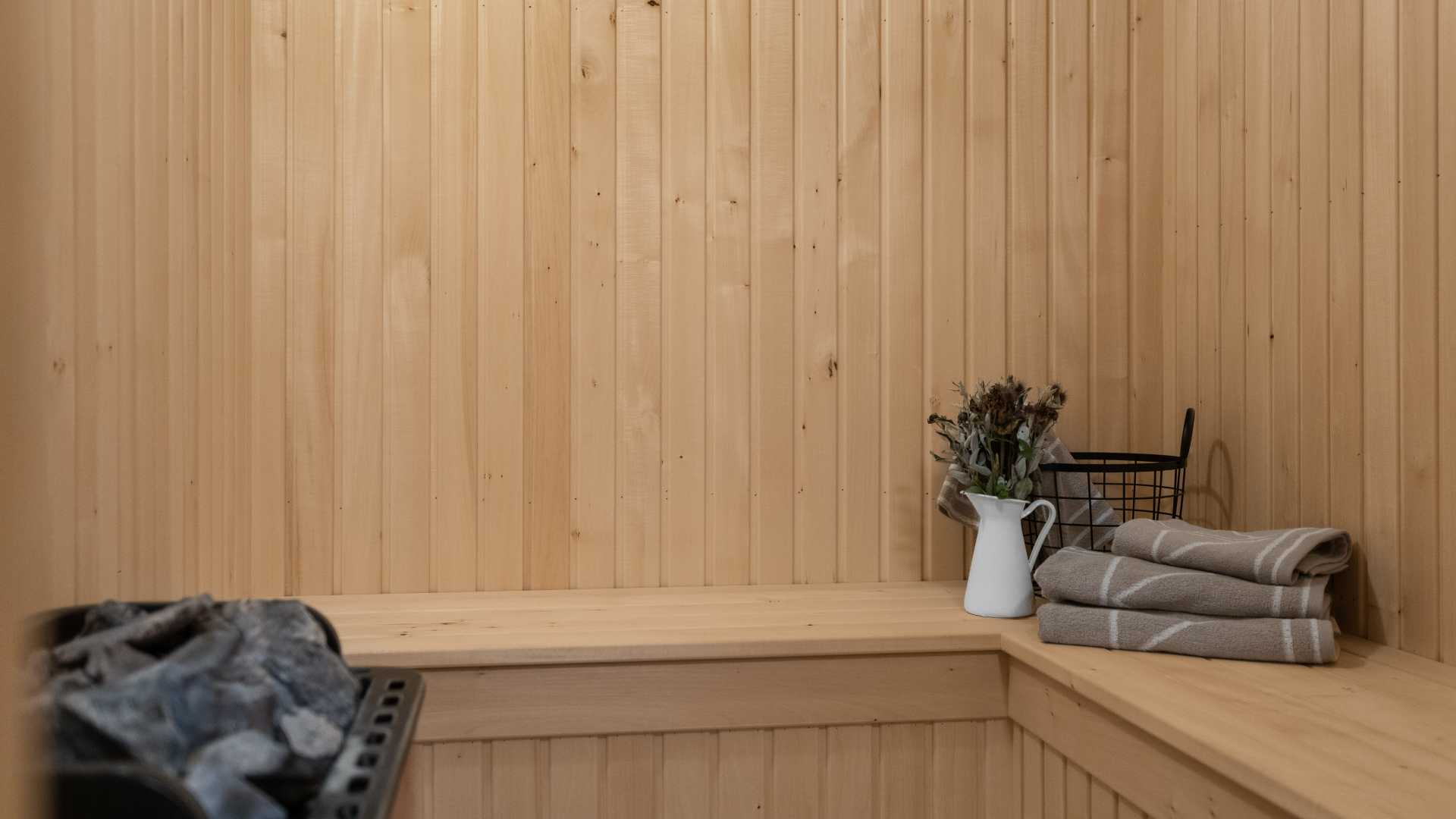 Koselig badstue med trepanelvegger, håndklær og en vase på benken, skaper en avslappende atmosfære.