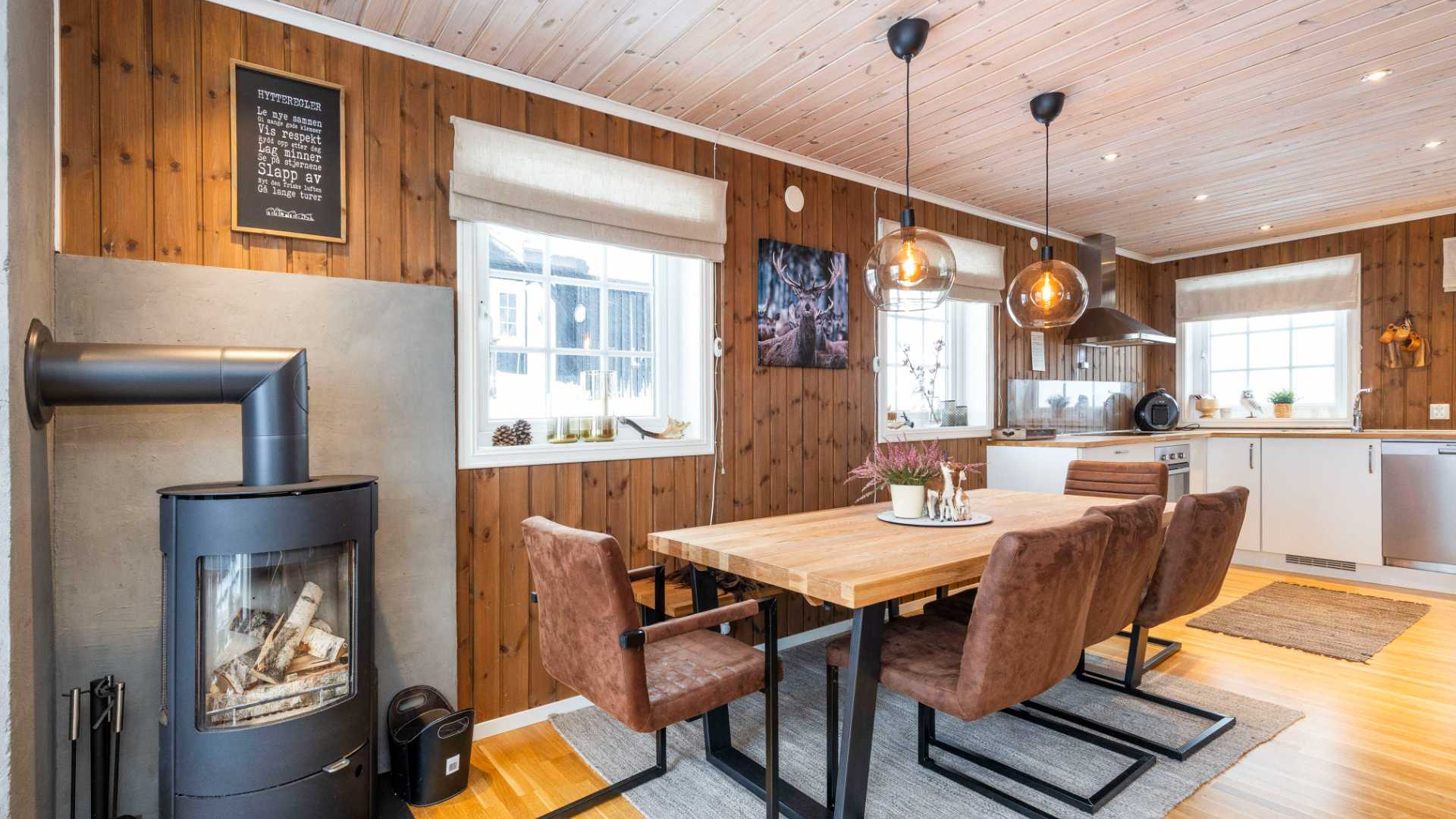 Koselig kjøkken og spisestue med peis, trevegger og moderne møbler i en hytte.