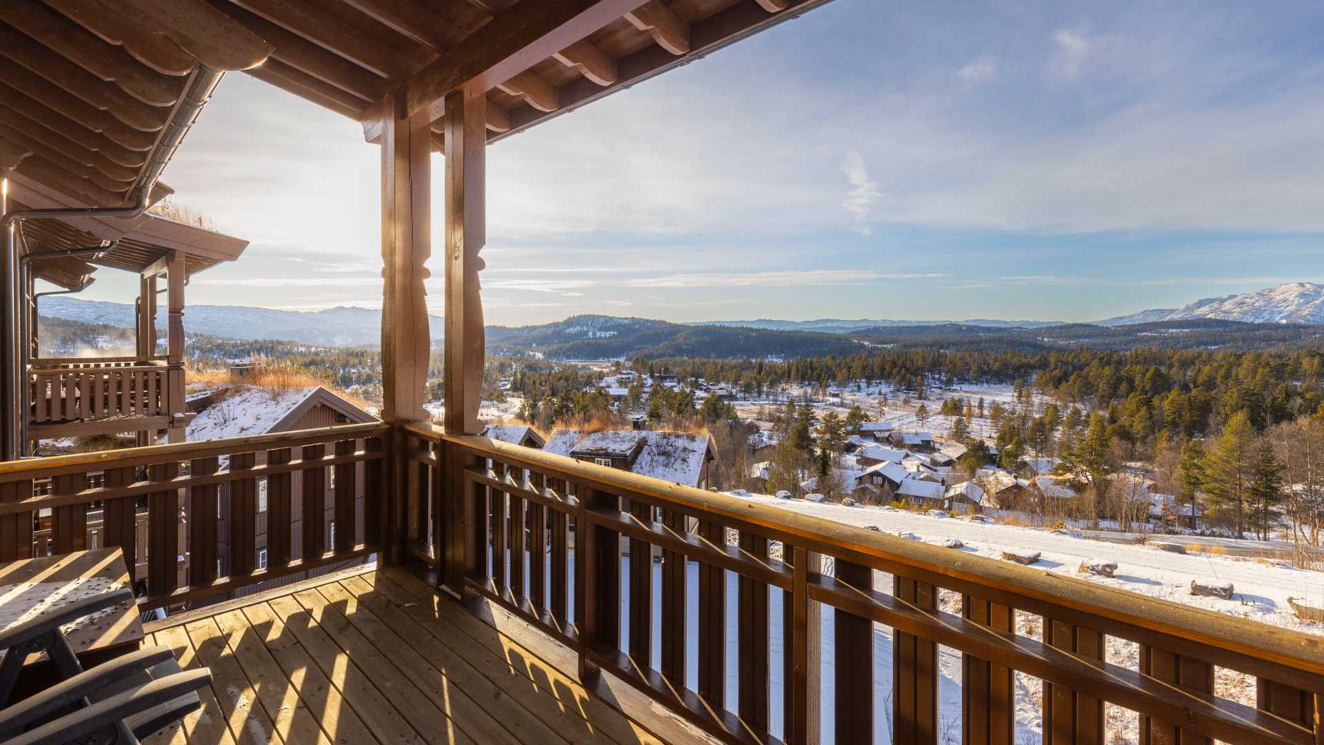 Utsikt fra en fjellbalkong over snødekt landskap og skog i Norge, med solrik himmel og fjell i horisonten.