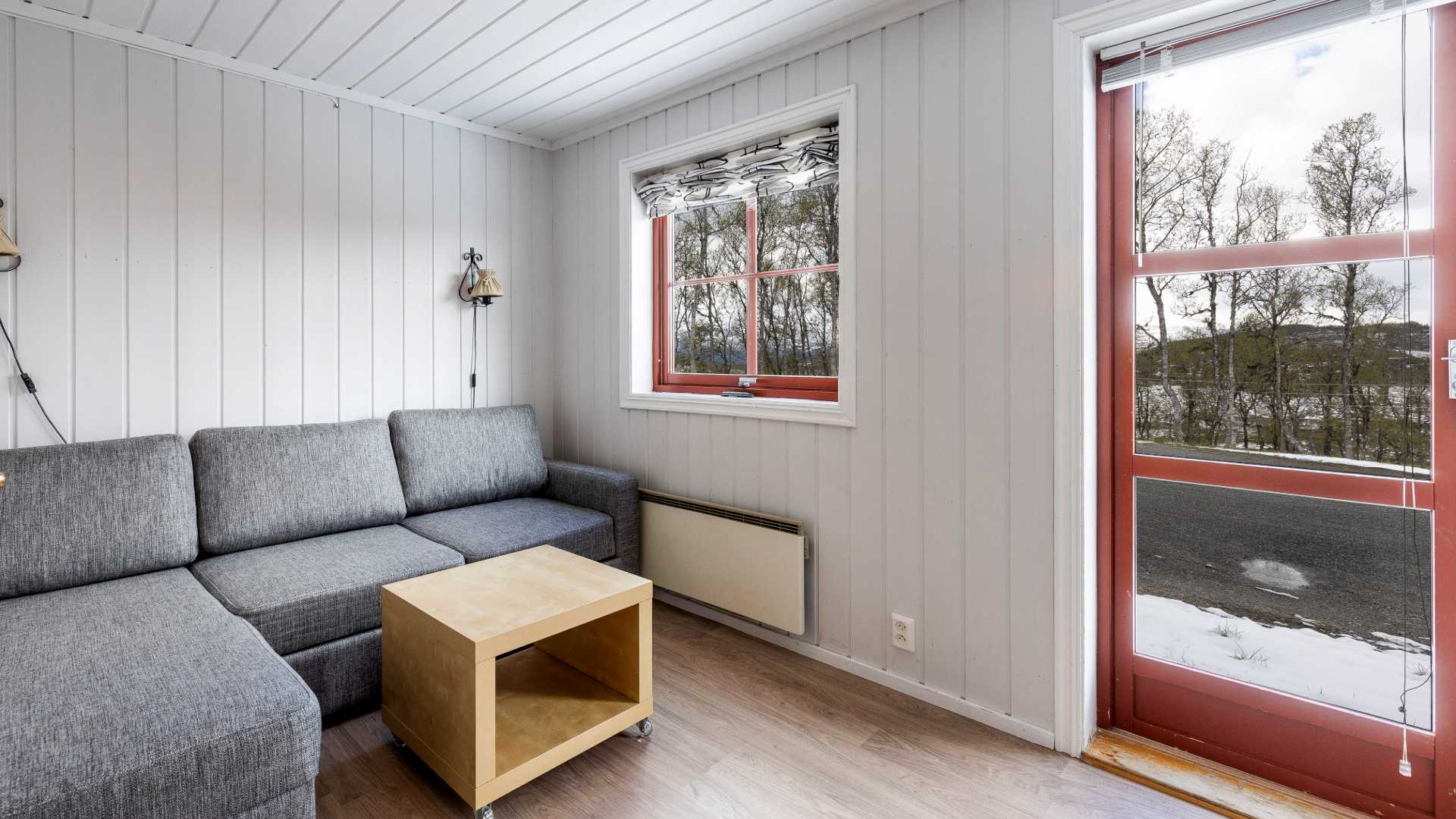 Lys stue med grå sofa, trebord og vindu som viser vinterlandskap utenfor.