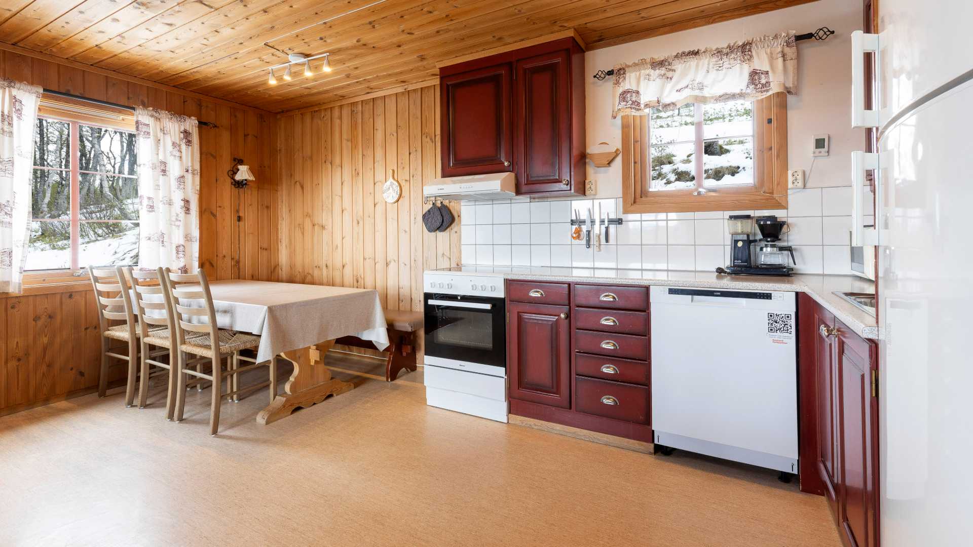 Koselig kjøkken med trepanel, spisebord og vindu med utsikt over vinterlandskap.