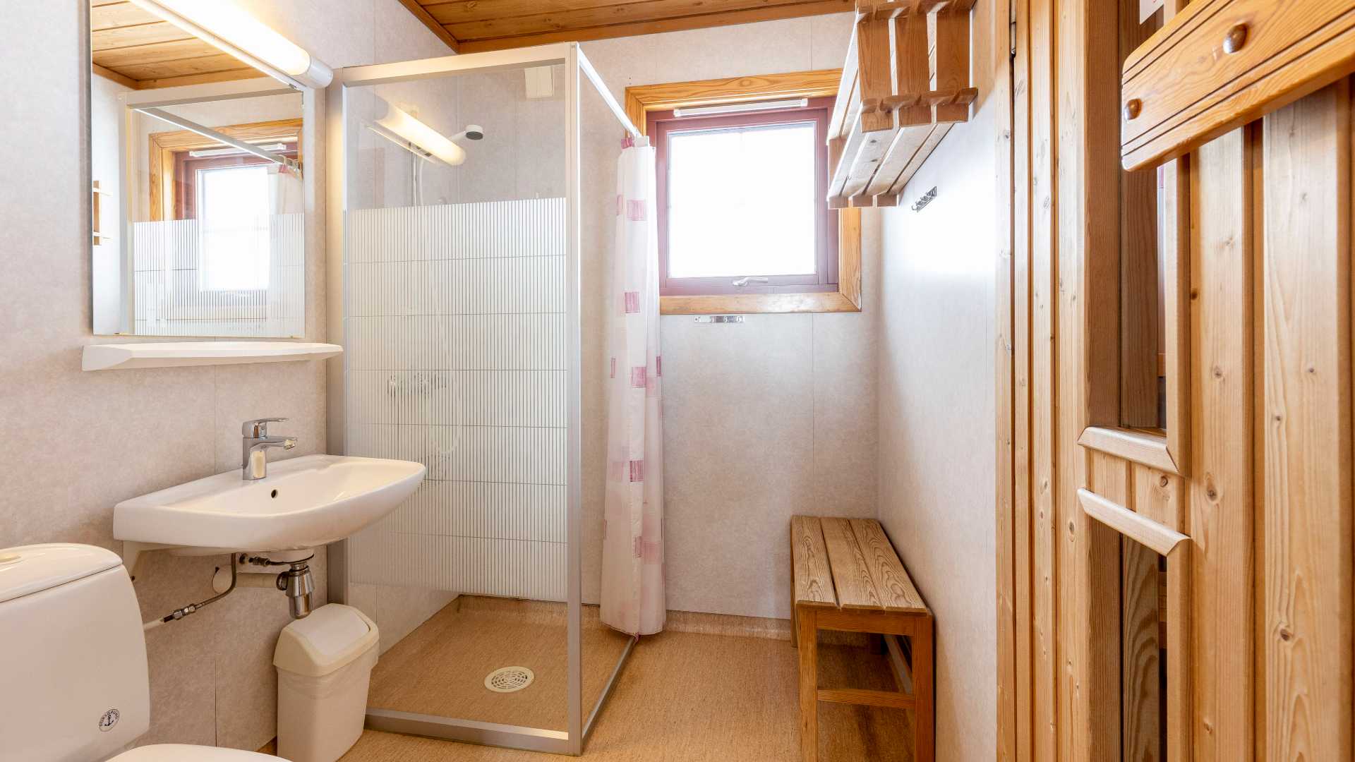 Lyst bad med dusjkabinett, servant, speil og treinteriør.