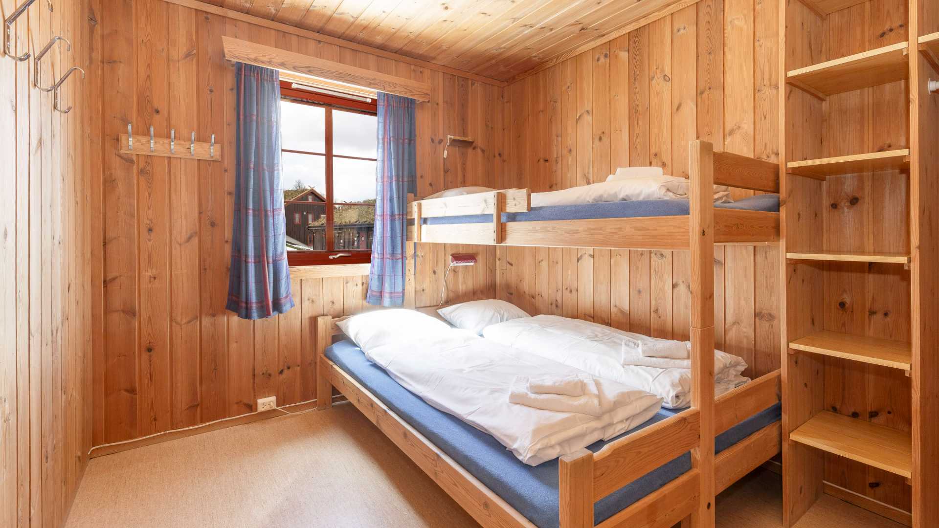 Koselig soverom med køyeseng i hytte, trepanel, og blå gardiner. Perfekt for familieferie på fjellet.