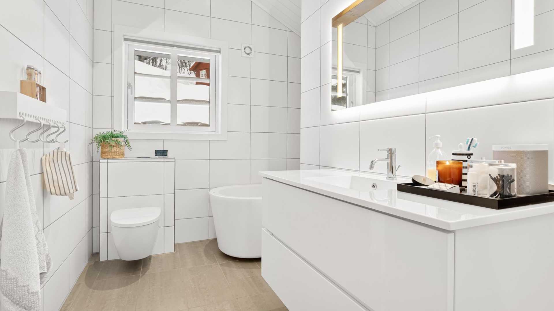 Moderne hvitt bad med servant, speil, badekar og vegghengt toalett. Lys og stilren design med planter.