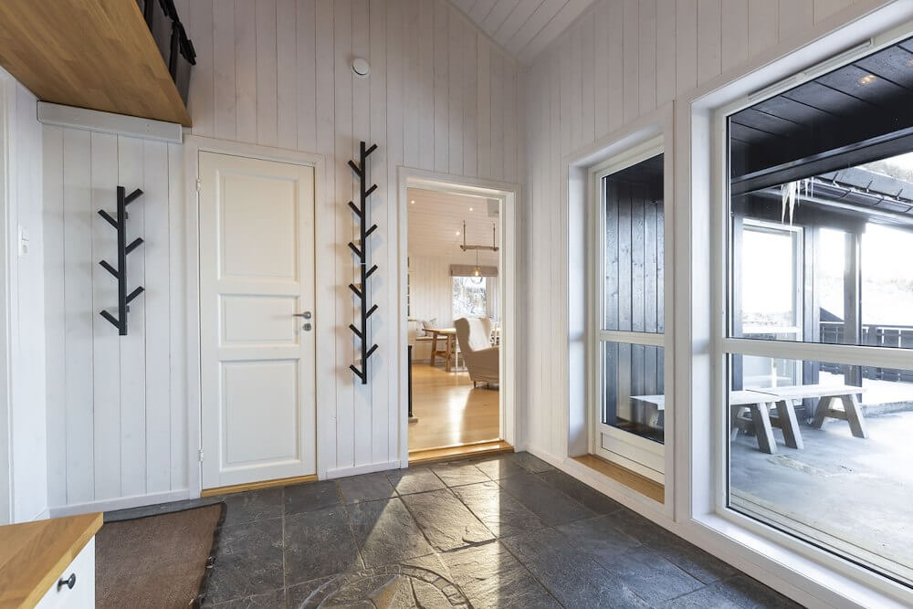 Lyst entréområde med store vinduer, moderne veggheng og tilgang til stue.