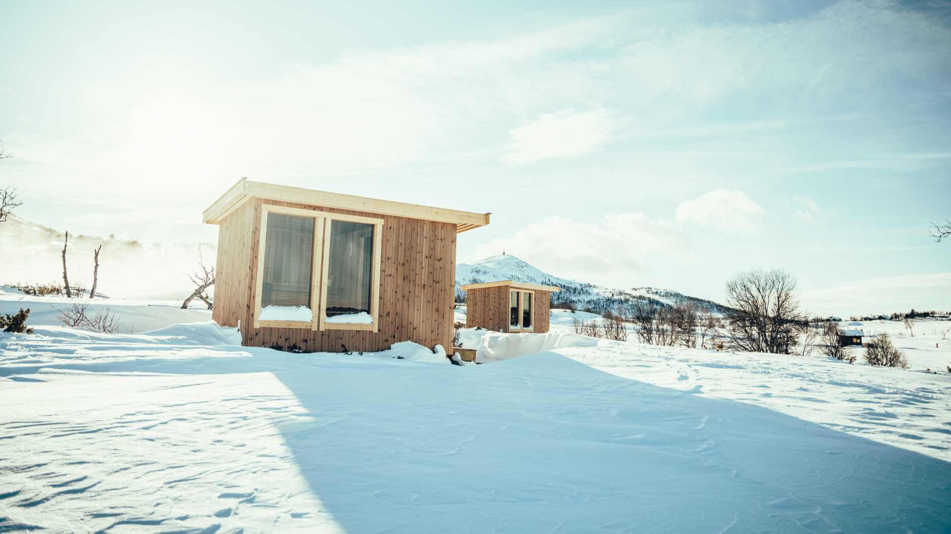 To små hytter i snødekt landskap med fjell i bakgrunnen under klar himmel.