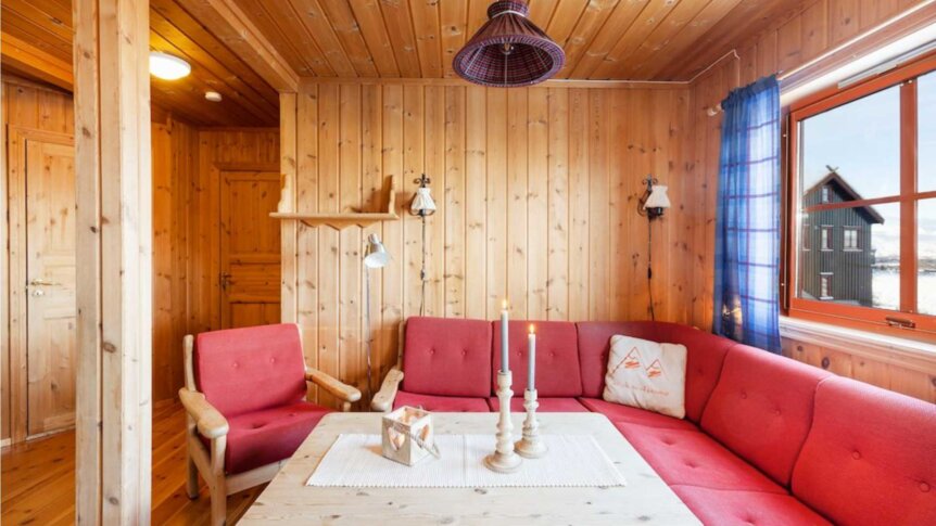 Koselig stue med trevegg, rød sofa, stearinlys og vindu med utsikt over landskapet. Perfekt for avslapning.