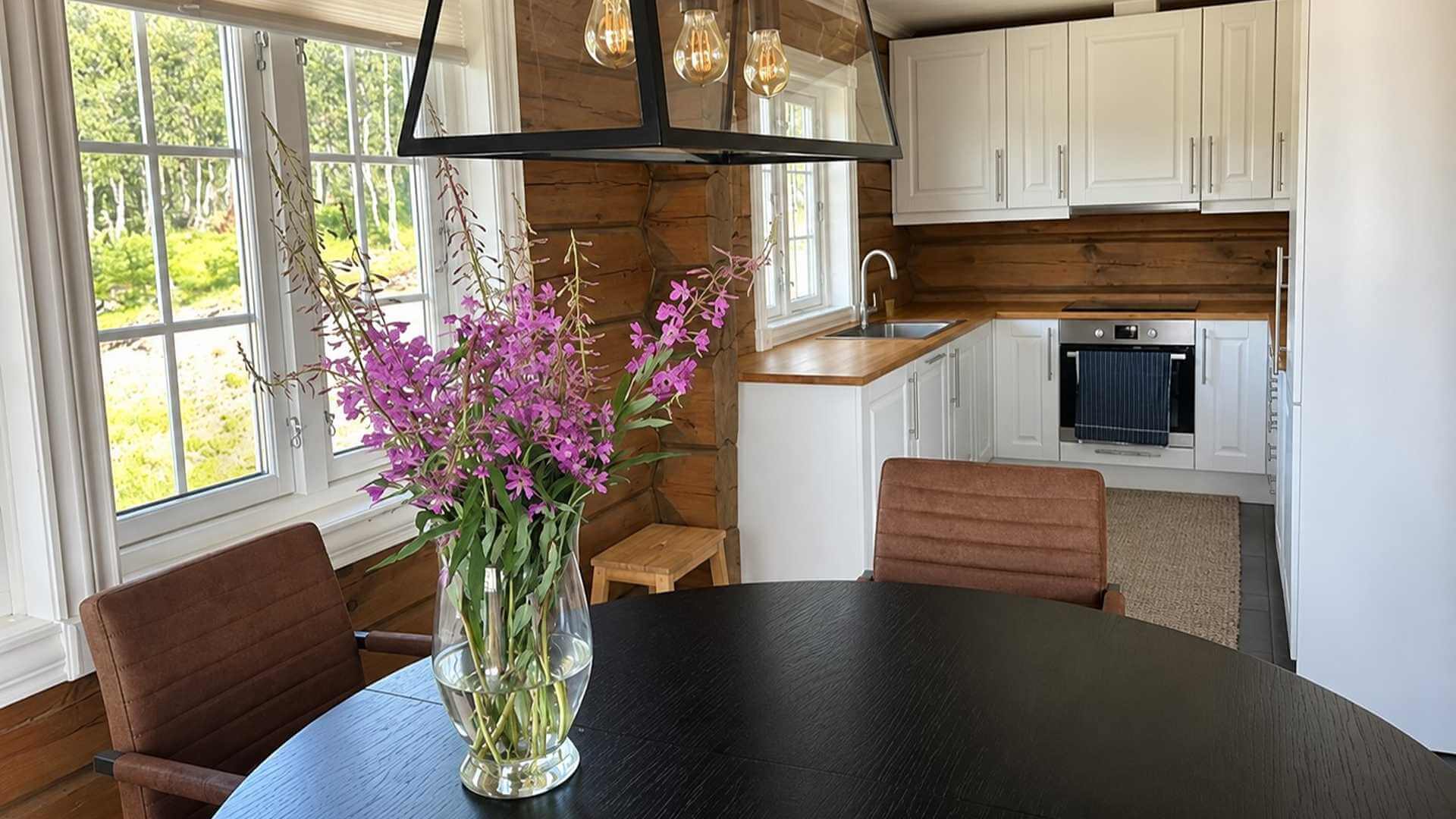 Lys og moderne kjøkken med bord, stoler og en vakker bukett lilla blomster. Perfekt for koselige måltider.