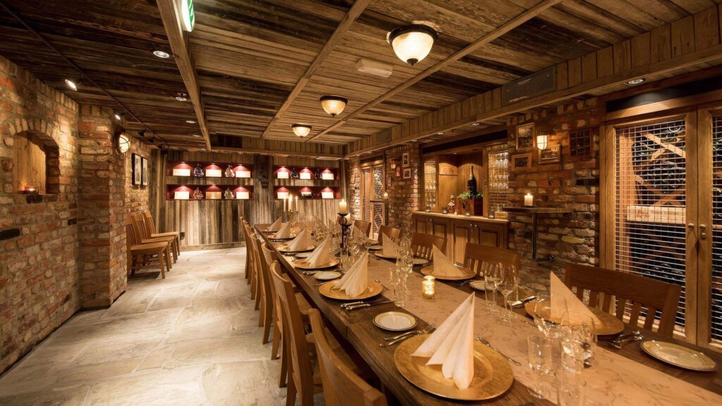 Koselig restaurant med langbord, steinvegger og varm belysning, klar for en intim middag.
