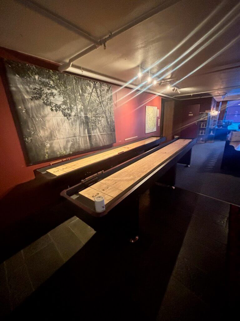 Innendørs spillrom med shuffleboard-bord, moderne belysning og kunstverk på veggen. Perfekt for underholdning.
