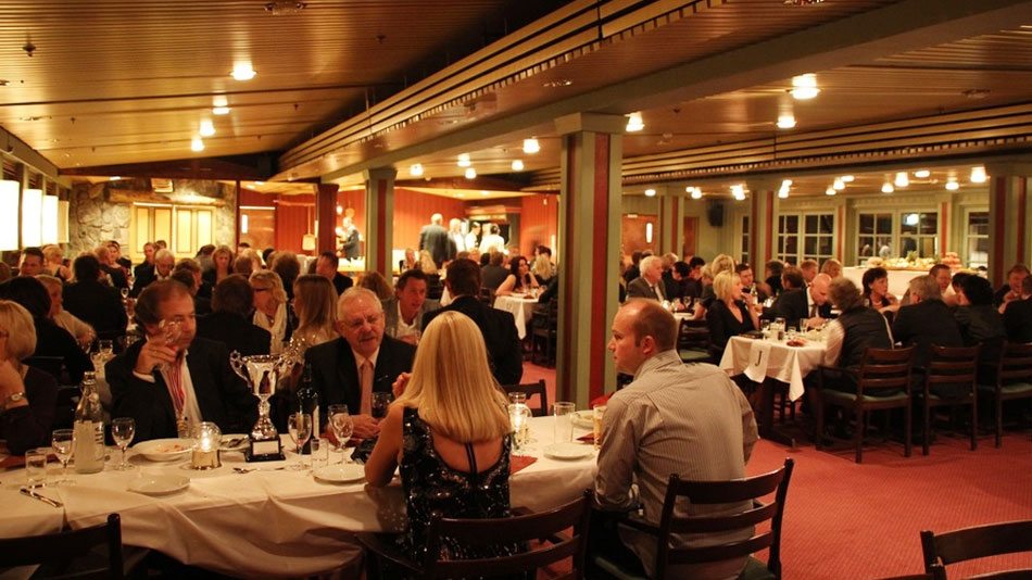 Middagsarrangement i en restaurant med mange gjester samlet rundt bordene.