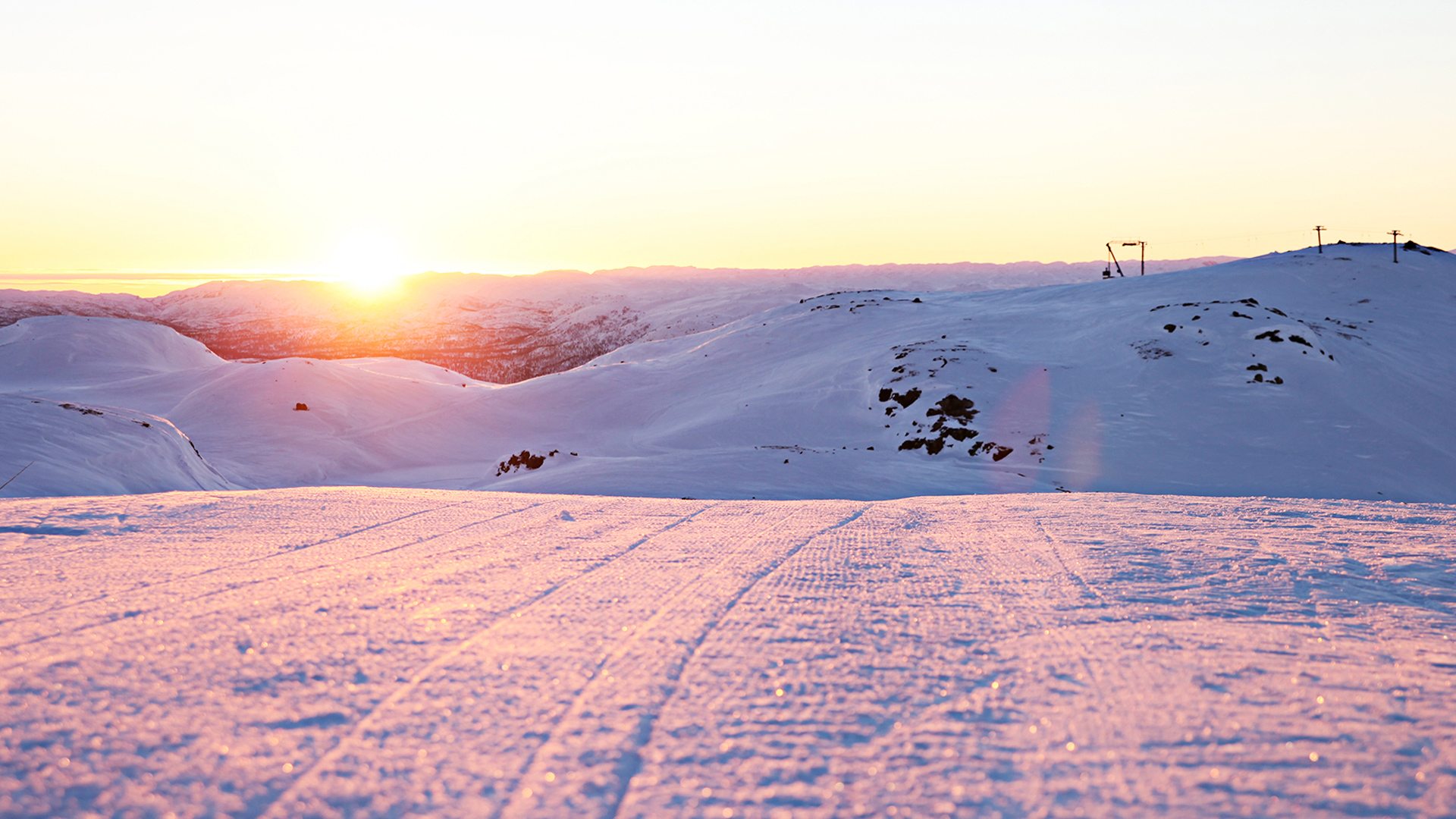 Solnedgang over snødekte fjelltopper i skianlegg, perfekt for vinterturisme i Norge.