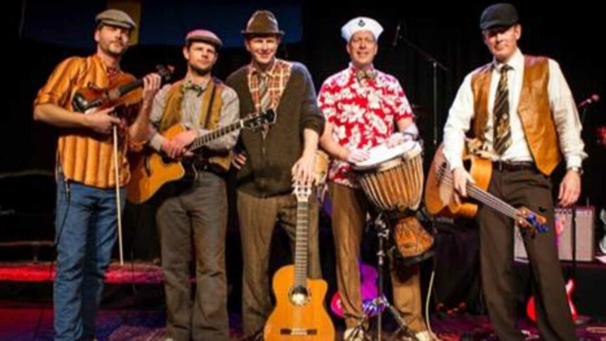 Fem musikere på scenen med gitarer, fiolin og tromme, alle iført uformelle klær og hatter.