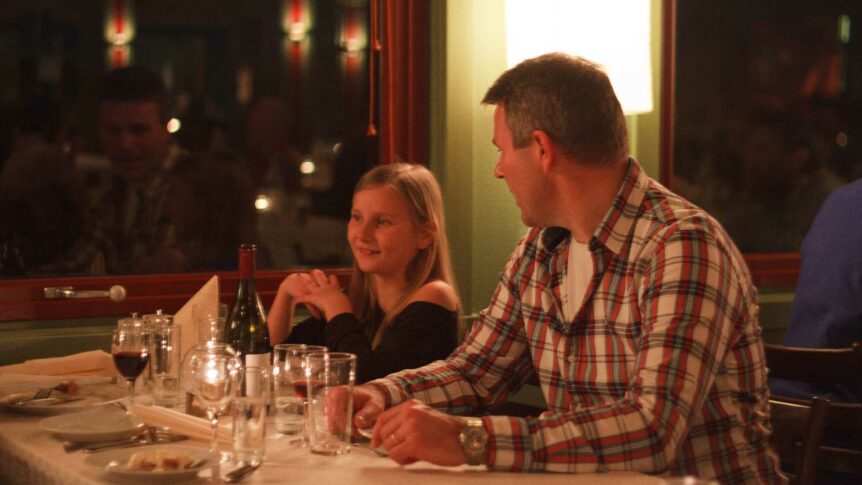 Mann og jente sitter ved et bord på en koselig restaurant, med vin og lys på bordet.