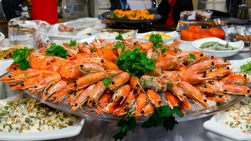 Reker på fat pyntet med persille på buffetbord med diverse tilbehør.