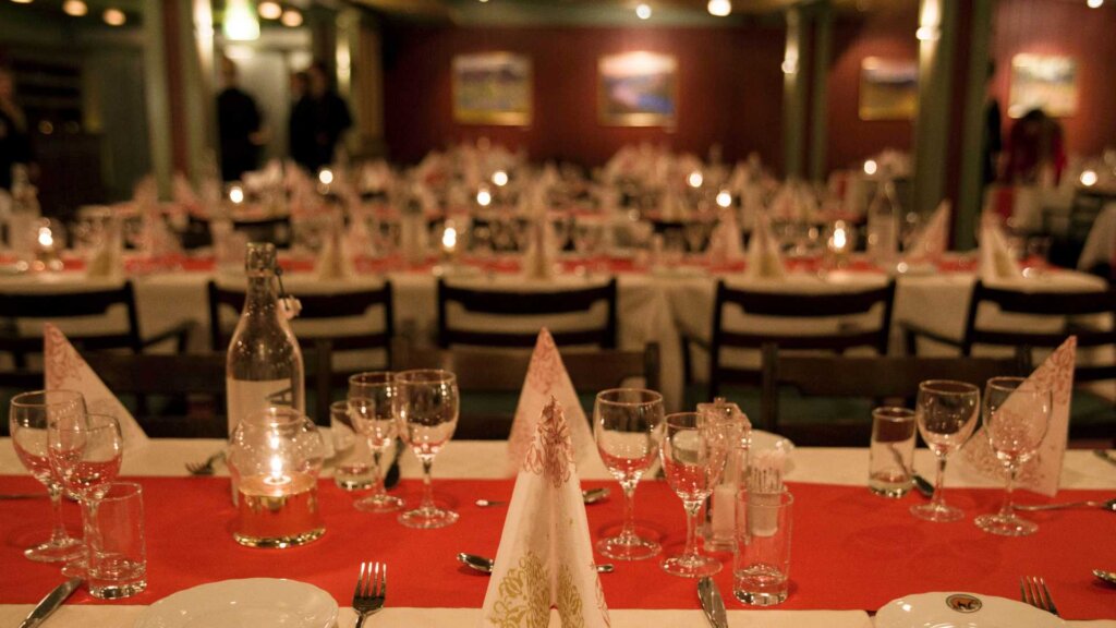 Oppdekking for middag med hvite duker, glass, lys og servietter i en elegant restaurantinnredning.