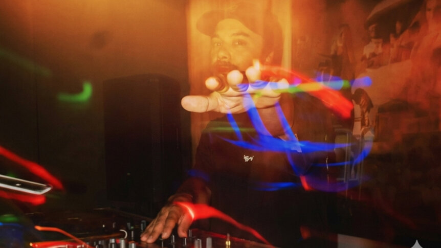 DJ spiller musikk i mørk klubb, fargerike lysstriper i bevegelse.