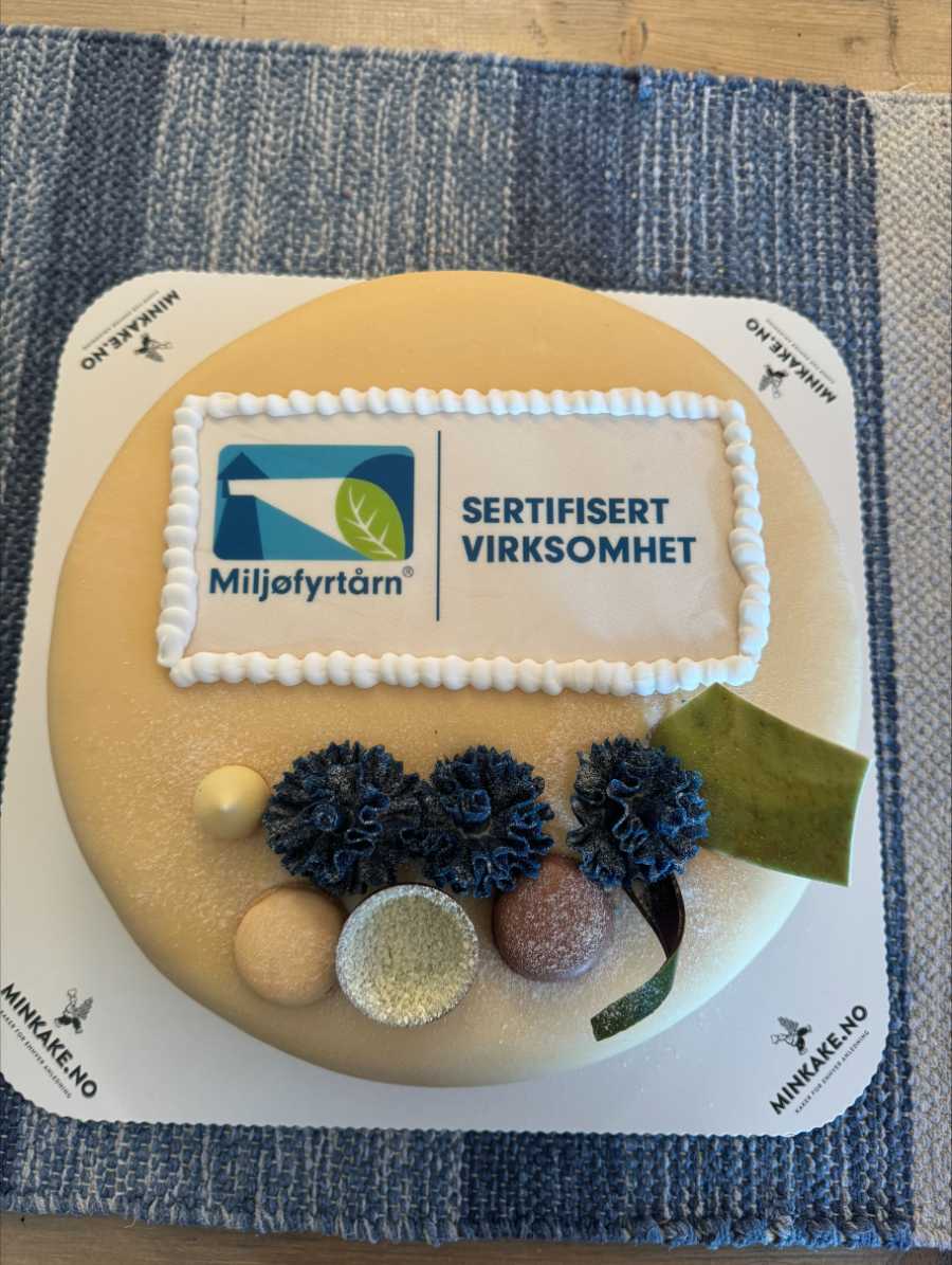 Kake med Miljøfyrtårn-logo og teksten Sertifisert virksomhet. Dekorert med blomster og kuler.