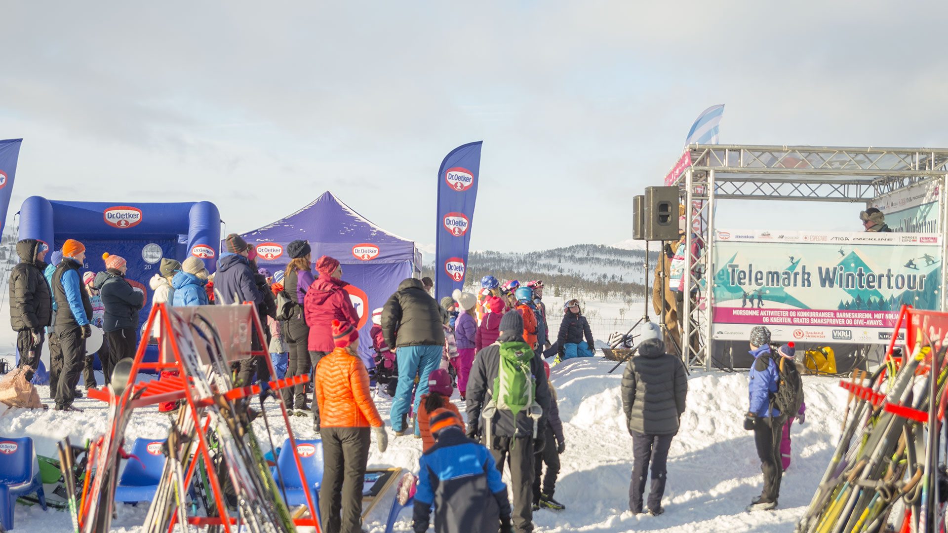 Vinterfestival med folk i varme klær samles ved Telemark Wintertour scene på snødekt landskap.