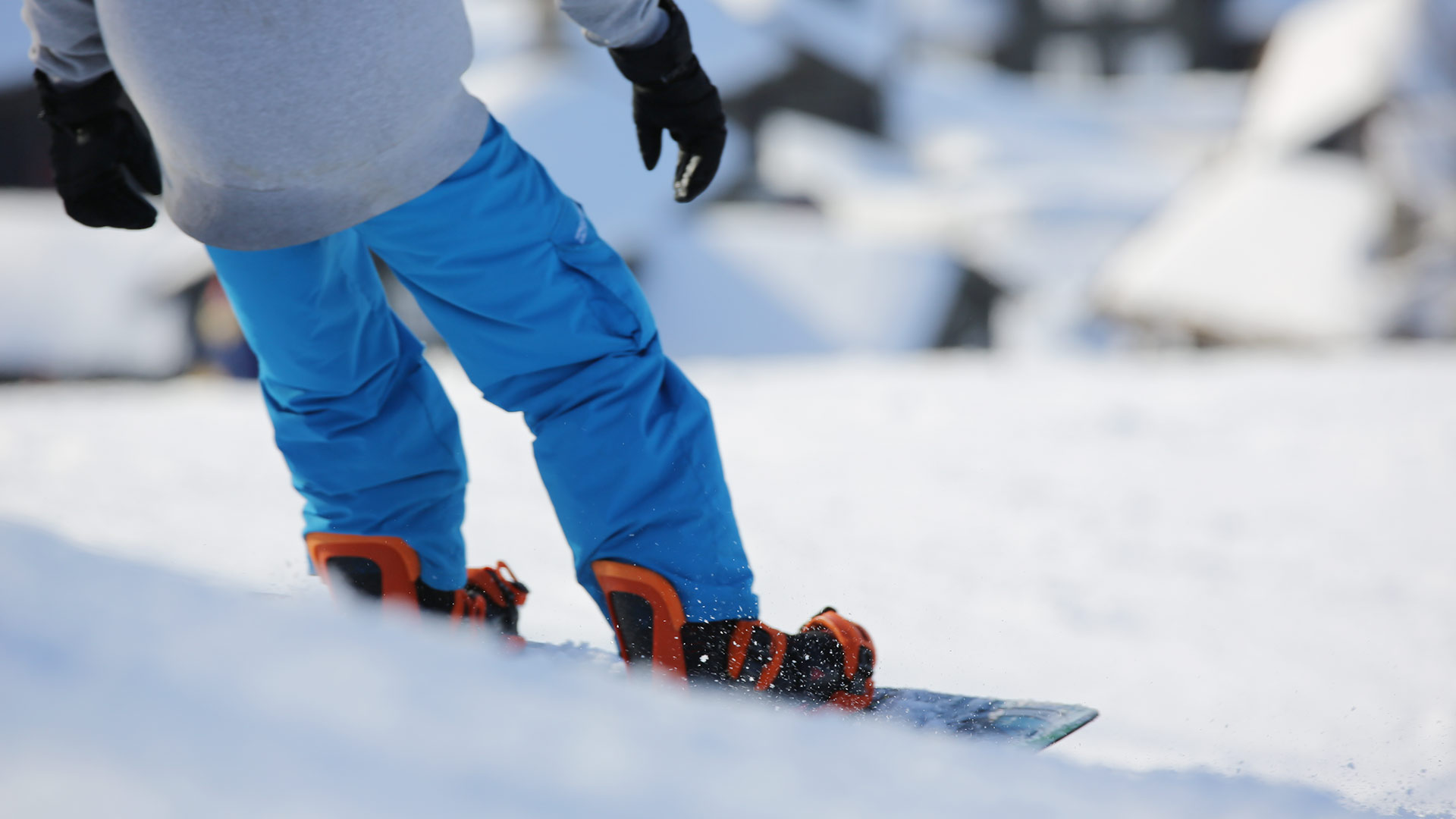 Person snowboarder ned snødekket bakke i fargerik vinterbekledning, nærbilde av nedre kropp.