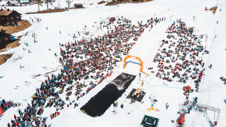 Stor folkemengde samler seg for skikonkurranse på vinterfestival med puddersnø og festlig atmosfære.