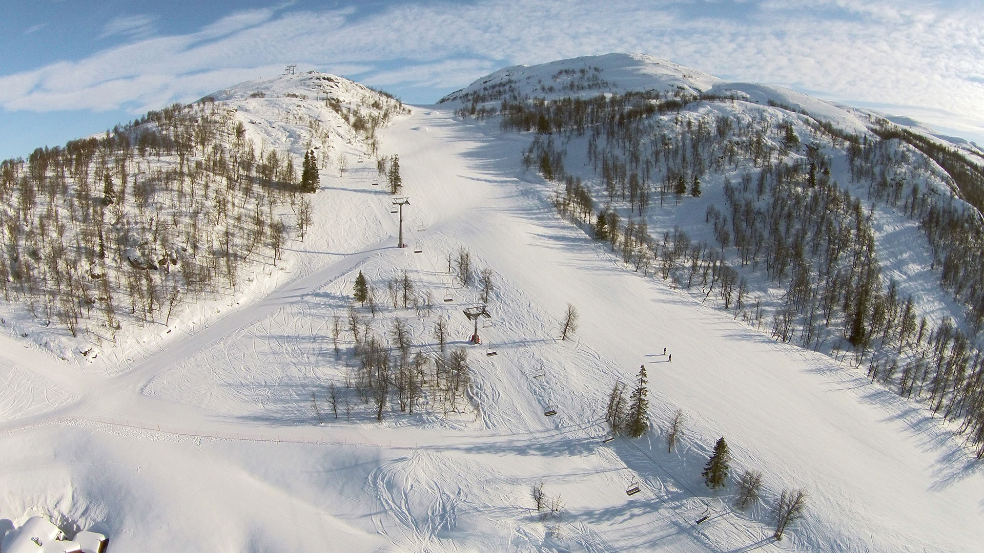 Snødekte, skogkledde fjell med skiheis og solfylt himmel, ideell for vintersport i Norge.