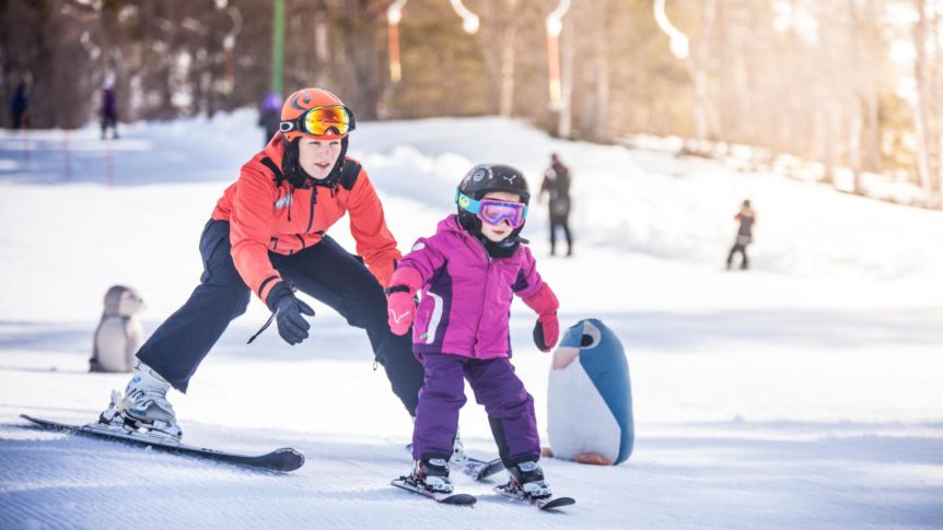 To mennesker på ski i en vinterscene, med en snøfigur i bakgrunnen.