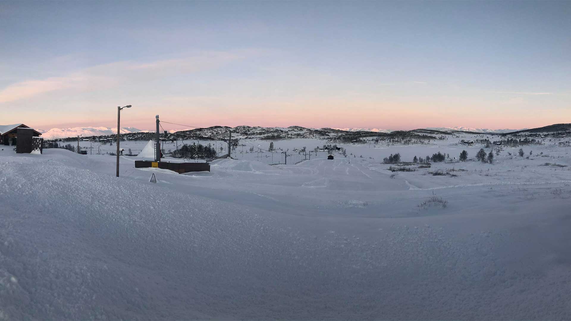 Snødekt landskap ved solnedgang i fjellene, med snøbelagte bakker og stille natur.
