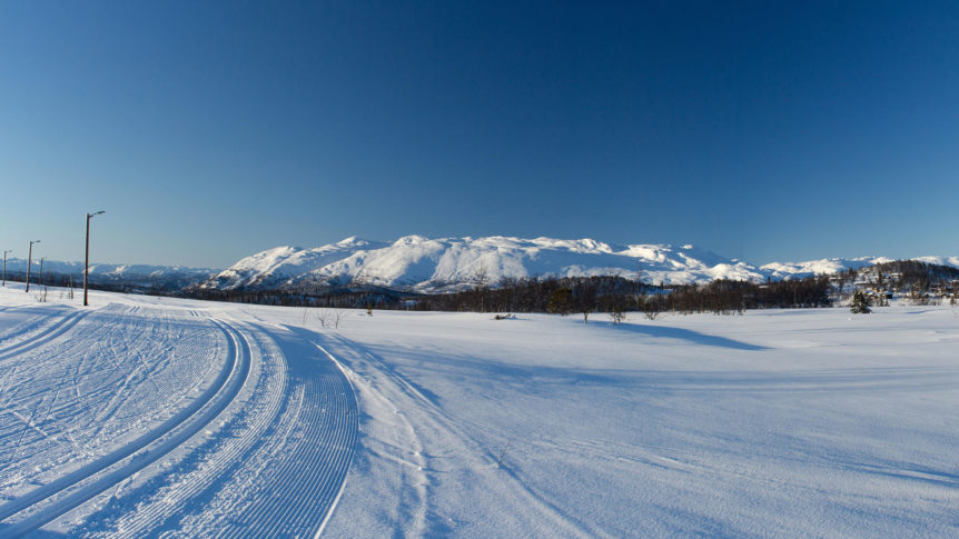 Snødekte fjell og preparerte skiløyper under en klar blå himmel i nydelig vinterlandskap.