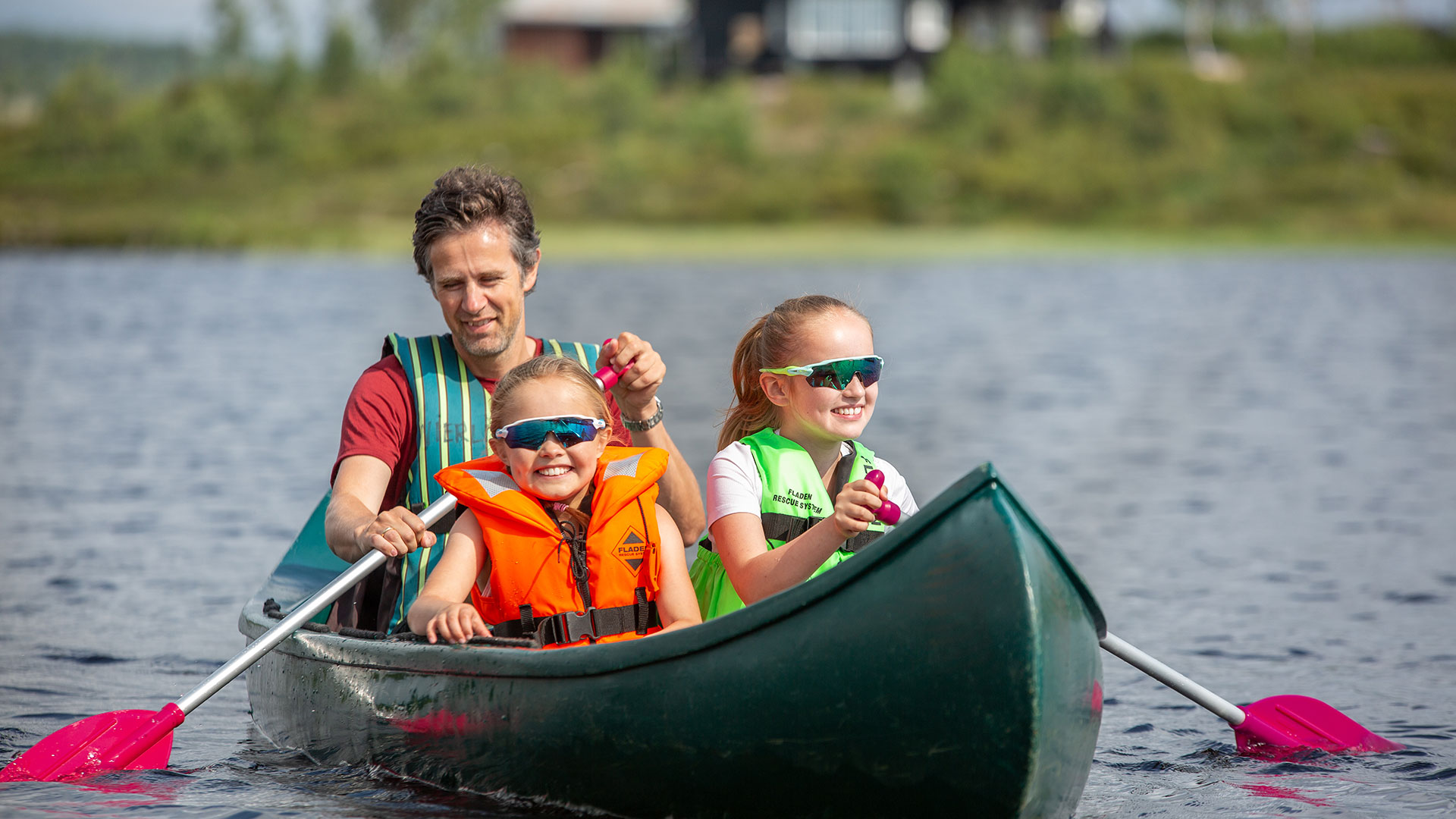Familie på kanotur med redningsvester og solbriller på en innsjø. Sommeraktiviteter og friluftsliv.