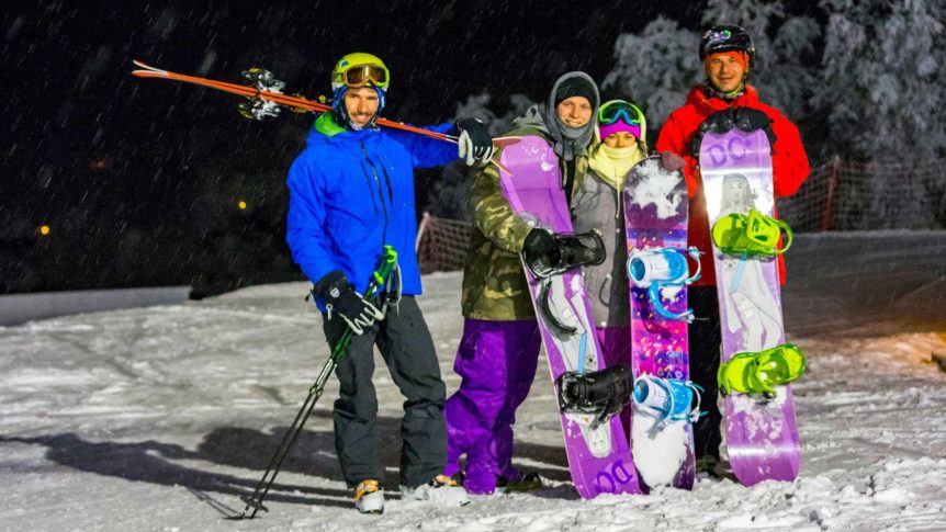 Fire personer med ski og snowboard nyter en snørik kveld på fjellet.