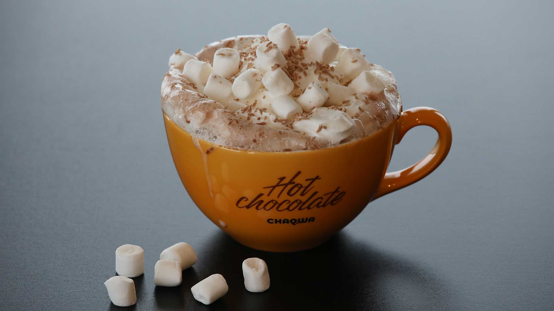 Varm sjokolade med marshmallows i en gul kopp på bordet. Perfekt for kalde dager.