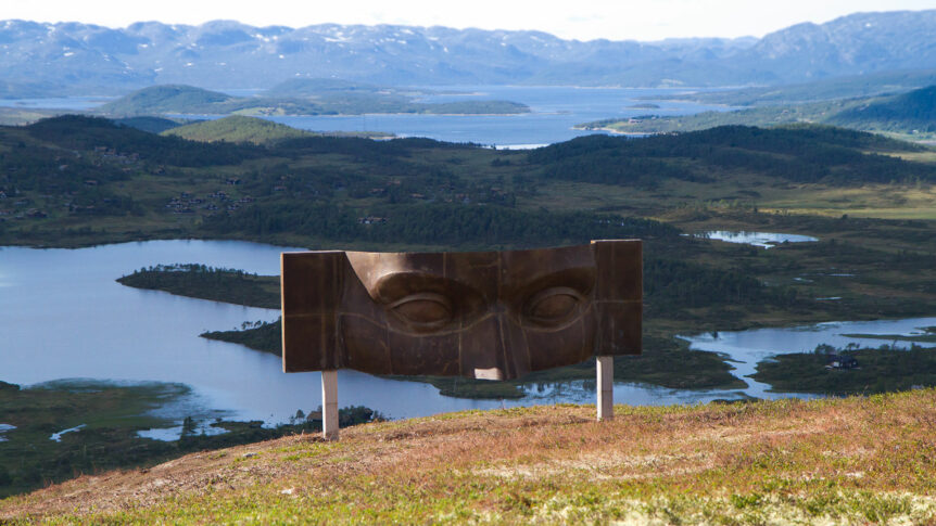 Skulptur av ansikt ved fjellutsikt over innsjøer og fjell i Norge.