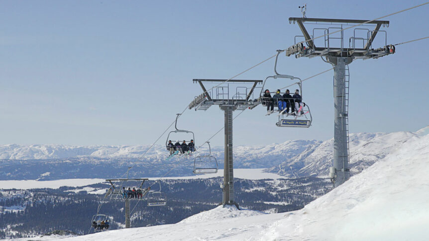 Folk i stolheis med snødekte fjell i bakgrunnen, solrik dag i skisenter, perfekt for vintersport.