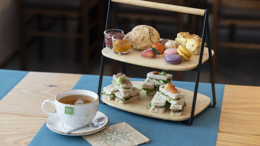 Afternoon tea med smørbrød og kake, servert på etasjefat, med kopp te på bord dekker med duk.