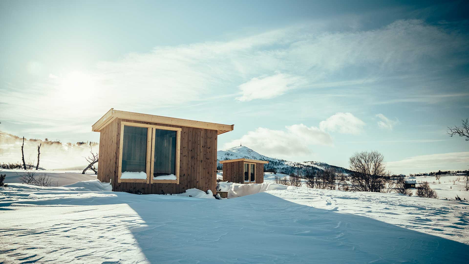 To små hytter i et snødekket fjellandskap under klar blå himmel.