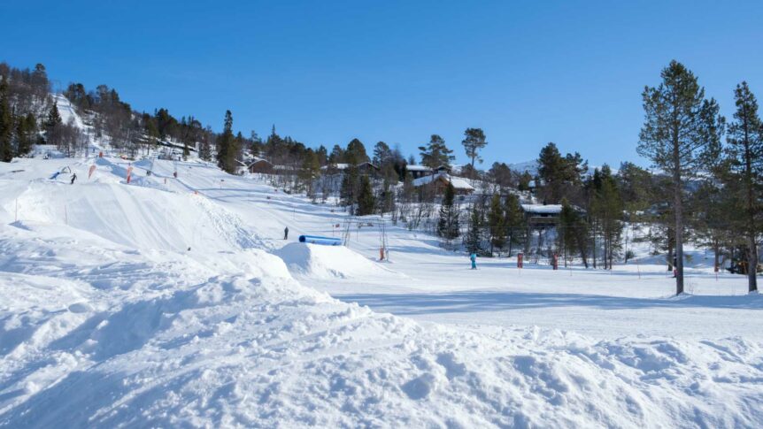 Snødekt skianlegg med bakker og trær under en klar blå himmel, perfekt for vintersport i Norge.