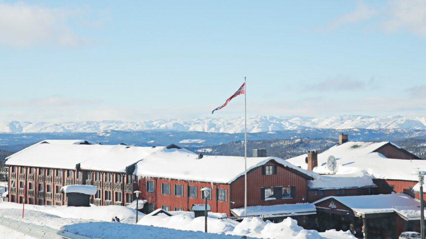 Rødt norsk fjellhotell dekket av snø, med fjell i bakgrunnen og norsk flagg vaier i vinden.